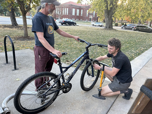 one individual holds a bike while another uses a tire pump