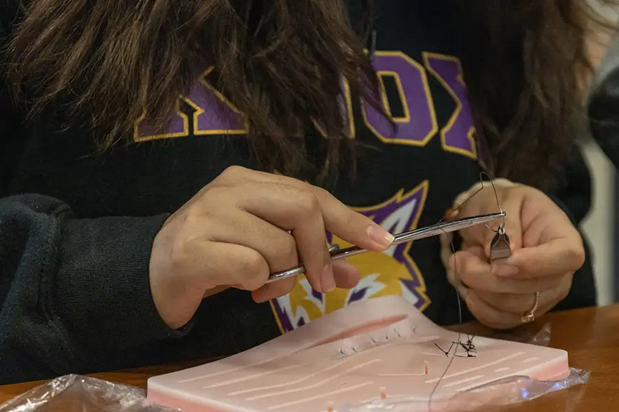 A close up of a students hand holding sutures. 