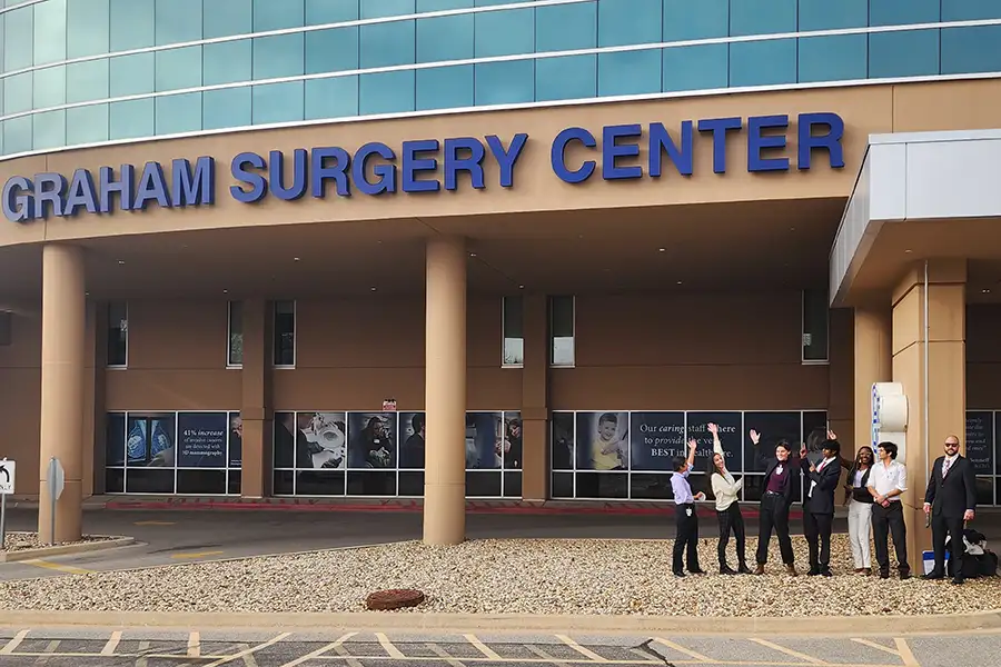 A group of students standing outside a building, pointing to the Graham Surgery Center.