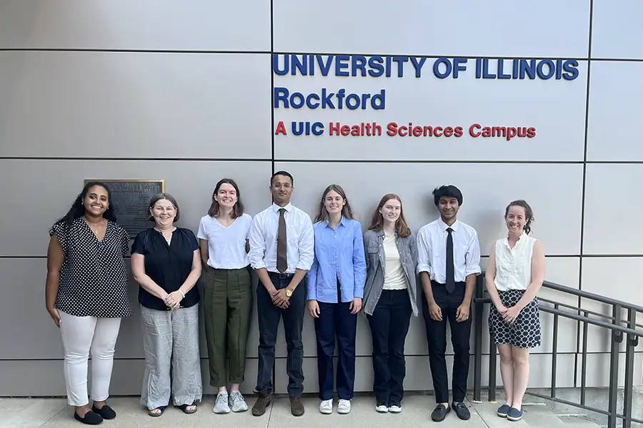 A group of students and advisors stand outside under a sign that reads University of Illinois Rockford A UIC Health Sciences Campus
