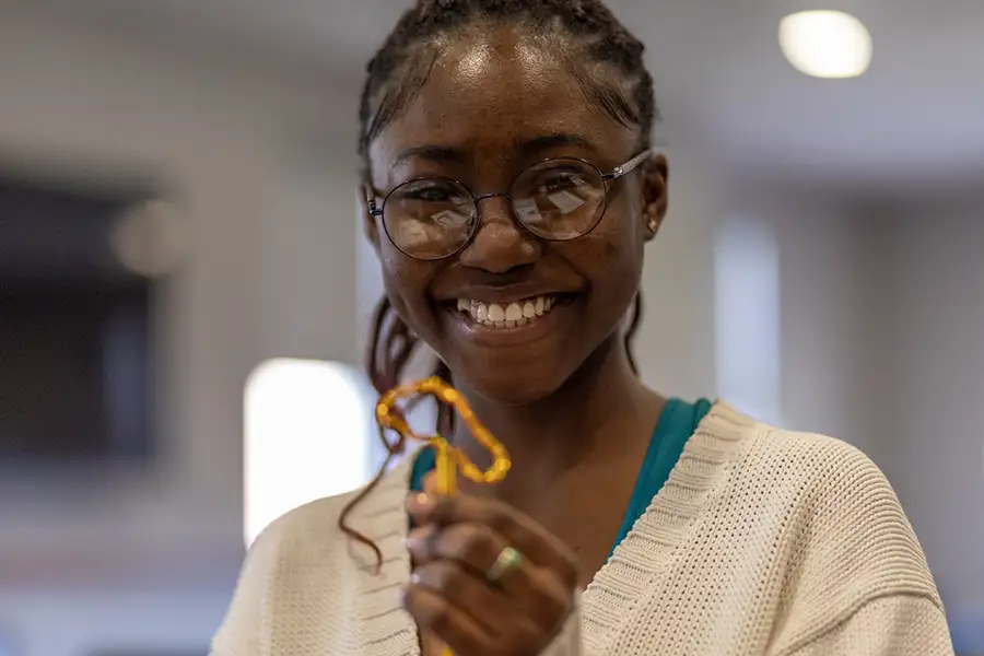 A student holding a think plastic foot, smiling at the camera.