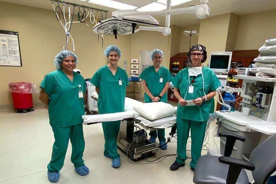 Four people stand next to an operation table, under the lights and in full scrubs.