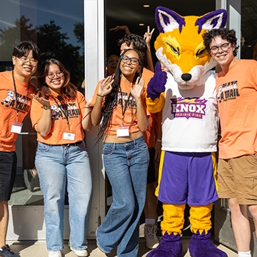 Four smiling Knox students pose with Blaze, the Prairie Fire Athletics mascot.