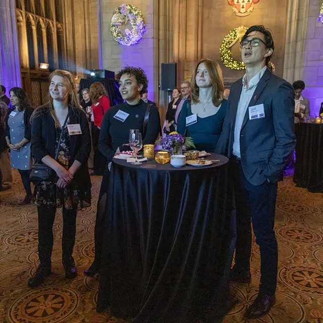 Chicago alums stand around a table while singing the Knox Hyme.