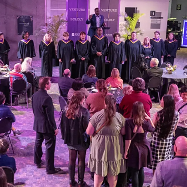 A group of alumni and friends gather in the event room to sing the Knox Hyme with the Knox Choir.