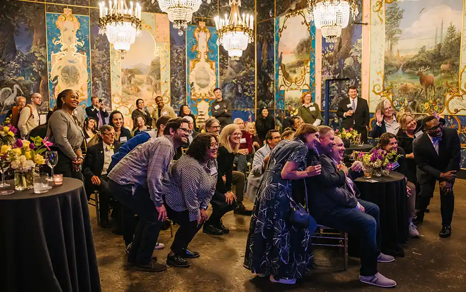 All attendees of the event smile from their tables as the speaker takes a selfie from the stage