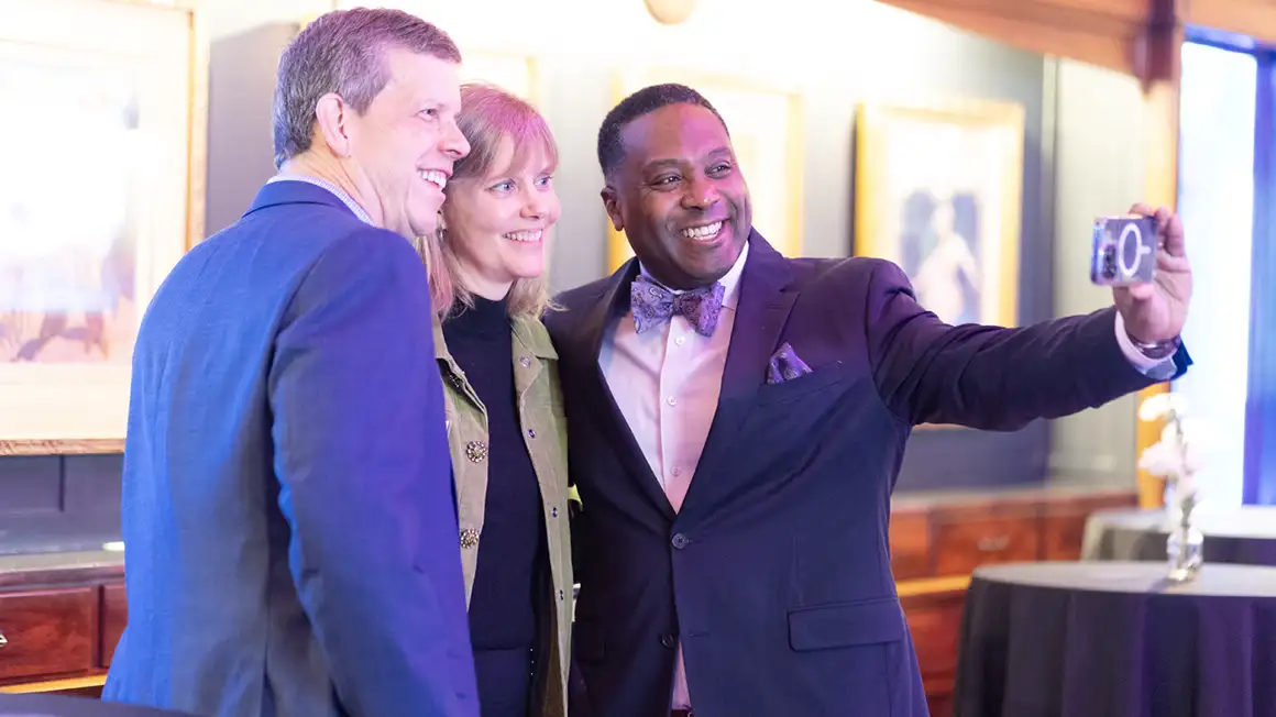 President C. Andrew McGadney poses with a couple while they all take a selfie together with President McGadney holding the phone.