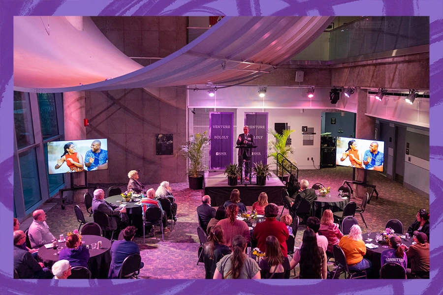 image of crowd gathered in a room with soft purple lighting, listening to Knox President C. Andrew McGadney speak 